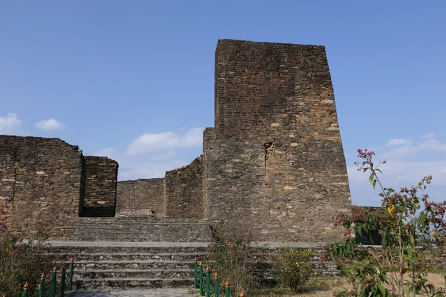 A tall square tower of dressed stone and low palace walls above a stone stair under a deep blue sky with a few clouds