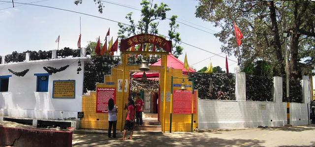 The yellow and red gateway of the Jhula Devi temple with bells hanging among trees