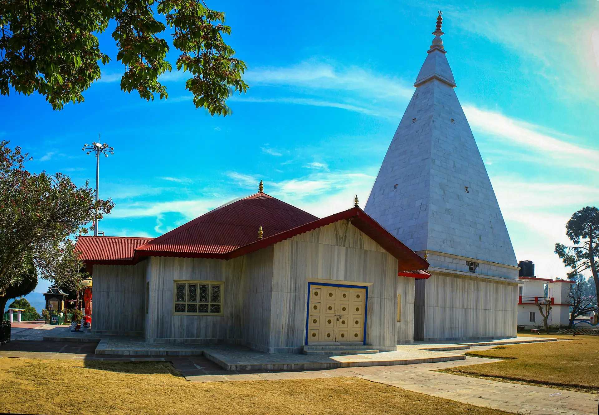 A white pyramid-roofed temple beside a red-roofed hall on the grass at the Haidakhan Temple