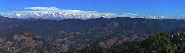 A wide panorama of forested ridges below a long line of snow-capped Himalayan peaks seen from Ranikhet