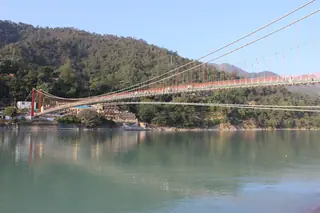 The Lakshman Jhula suspension bridge with red-painted cables crossing the green Ganges below forested hills