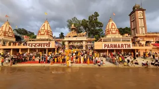 The ghat at Parmarth Niketan at dusk, with a crowd on the steps and the ashram's towers and clock tower behind