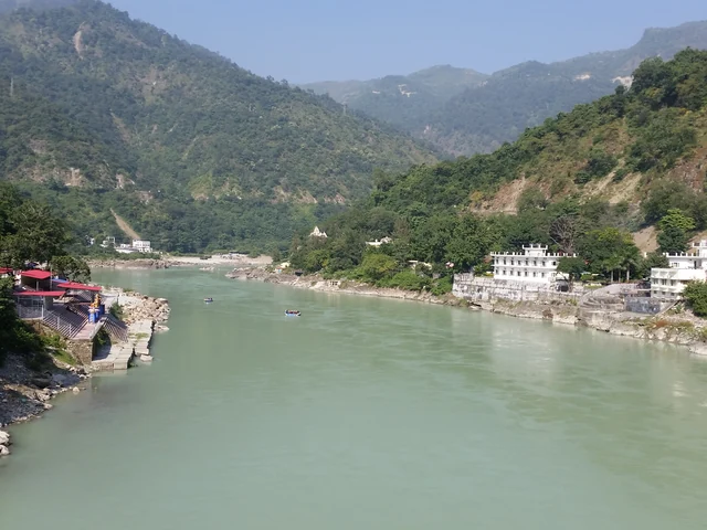 The green Ganges flowing between forested hills at Rishikesh, with buildings on the left bank