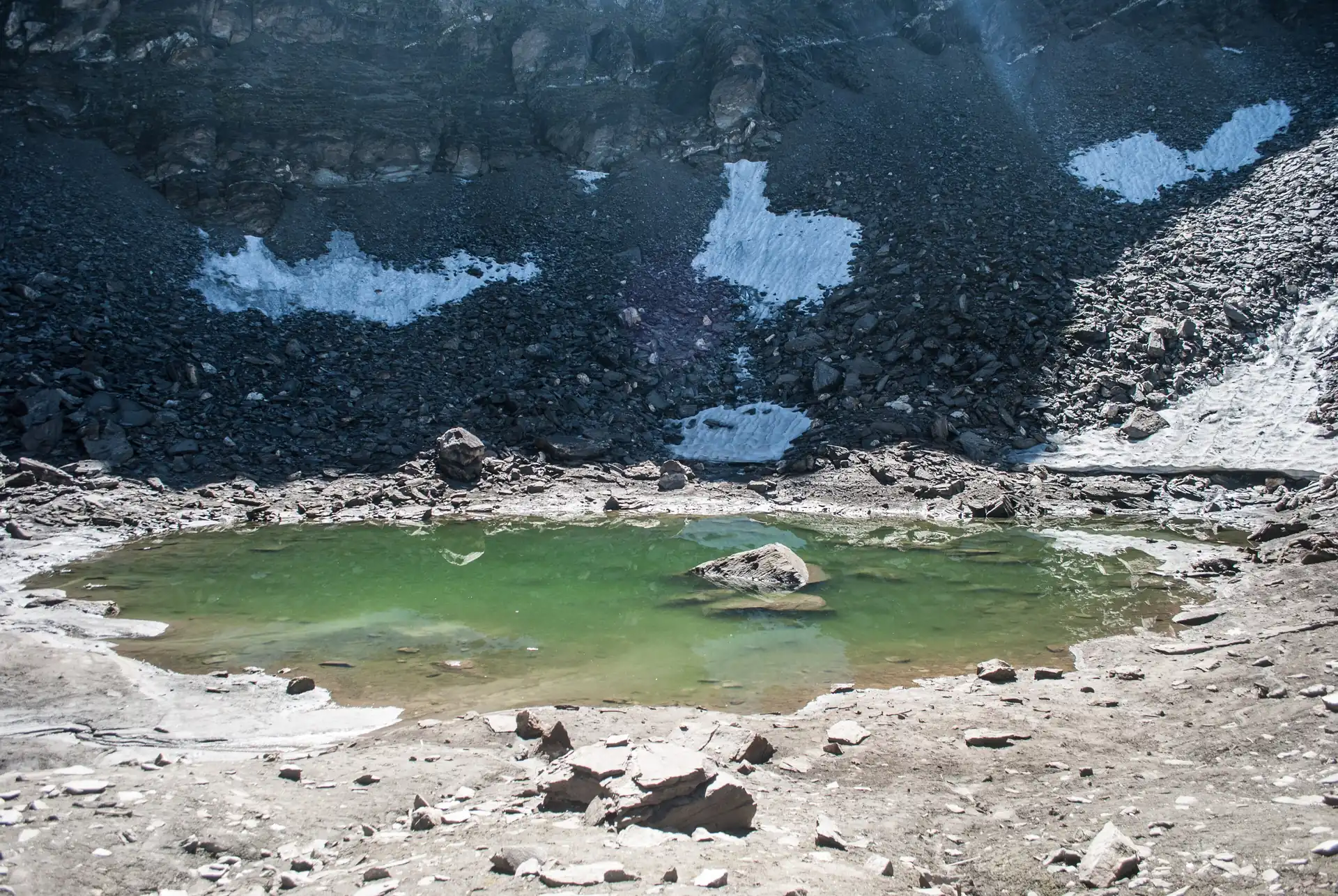 Roopkund, a small green glacial lake in a bowl of grey scree and old snow