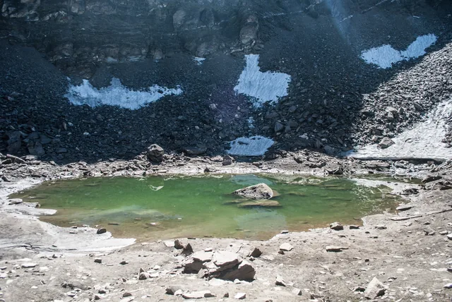 Roopkund, a small green glacial lake in a bowl of grey scree and old snow