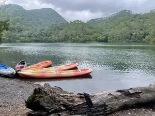 Brightly coloured kayaks on the stony shore of Sattal lake, with green forested hills and a cloudy sky behind