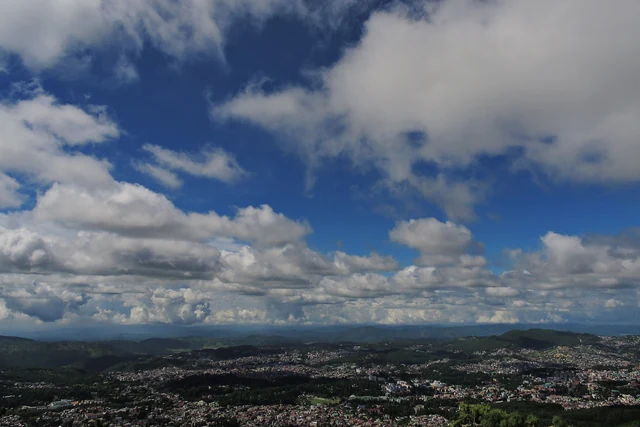 A wide view over the houses of Shillong spread across forested hills under a sky of towering white clouds