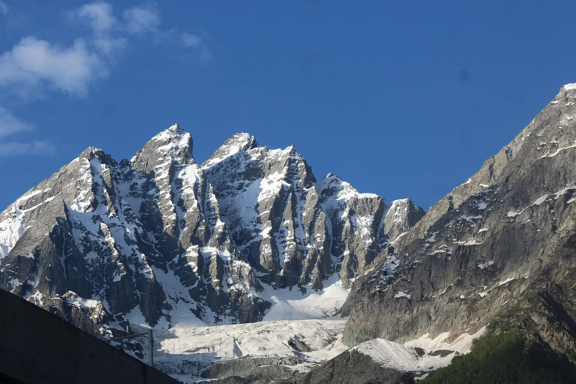 Jagged snow-streaked rock peaks above the grey tongue of a glacier on a clear blue day above Sonamarg