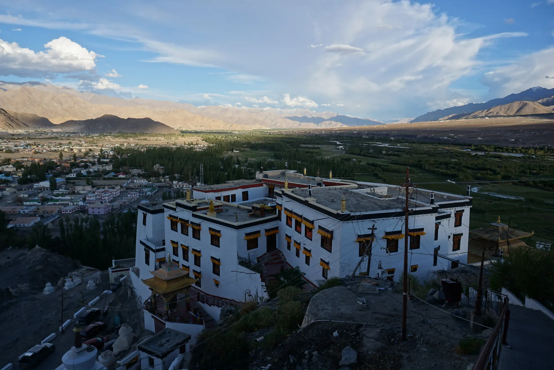 The white buildings of Spituk Monastery on a rocky hilltop above fields and a town in a wide valley