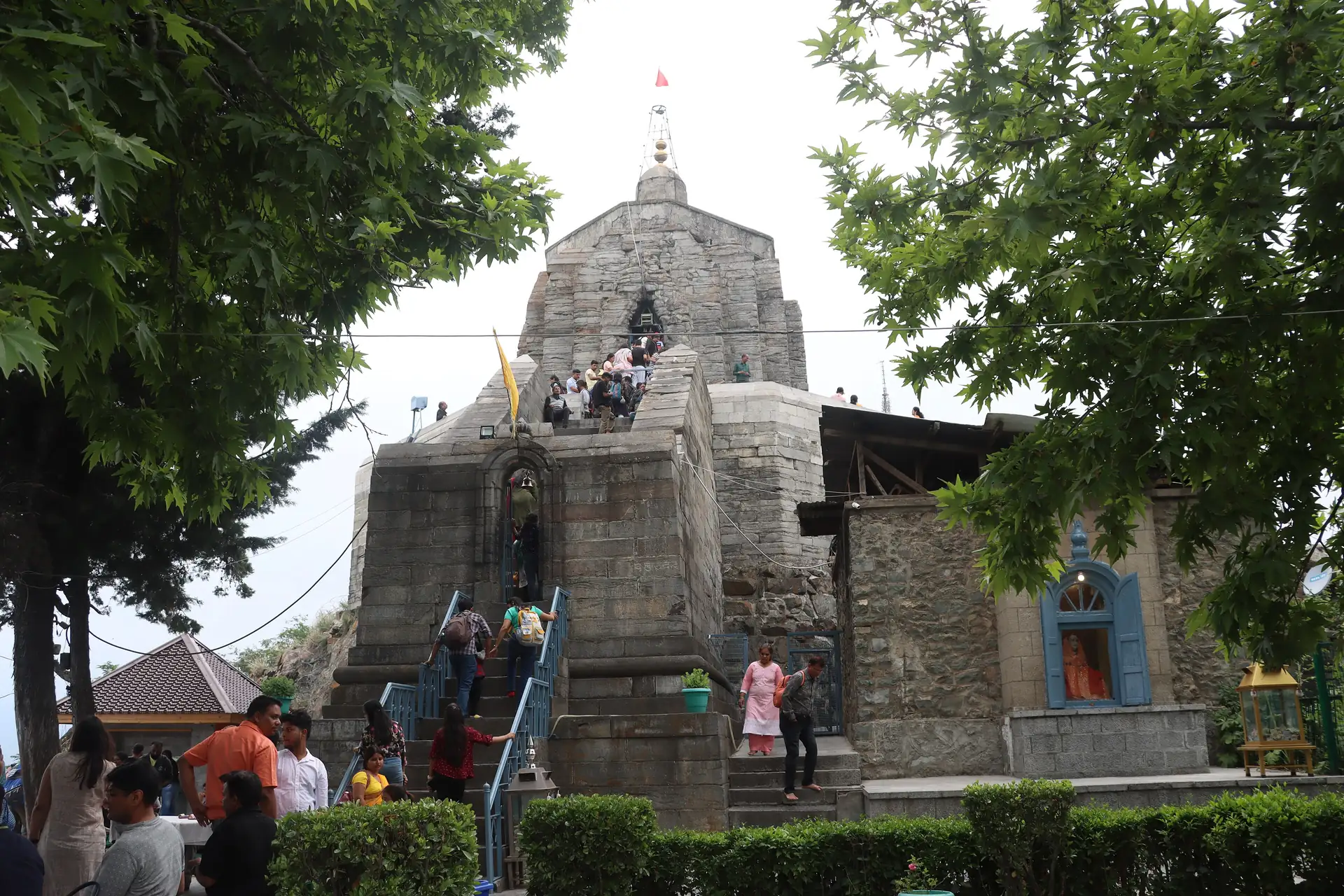 The grey stone Shankaracharya Temple on its hilltop with visitors climbing the steps among green trees