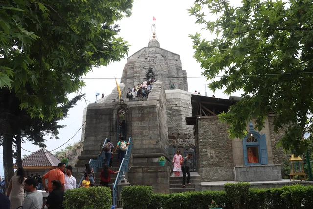 The grey stone Shankaracharya Temple on its hilltop with visitors climbing the steps among green trees