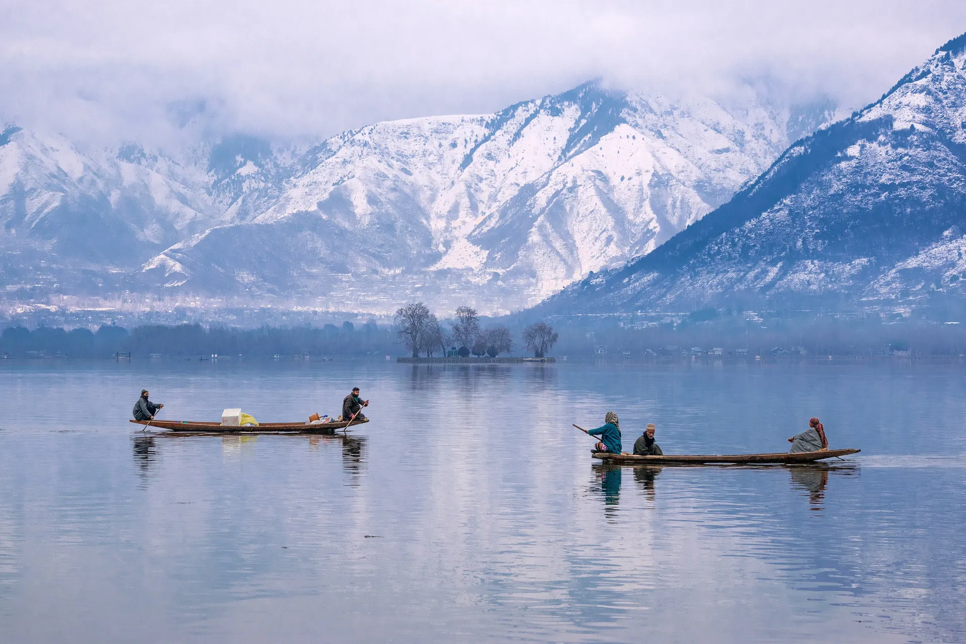 Two shikara boats on calm Dal Lake with snow-covered mountains rising behind the far shore