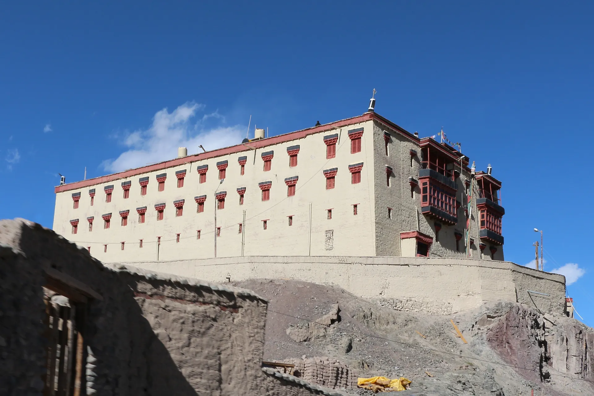 The long white palace building with a red-brown upper storey and small windows on a rocky rise under a blue sky
