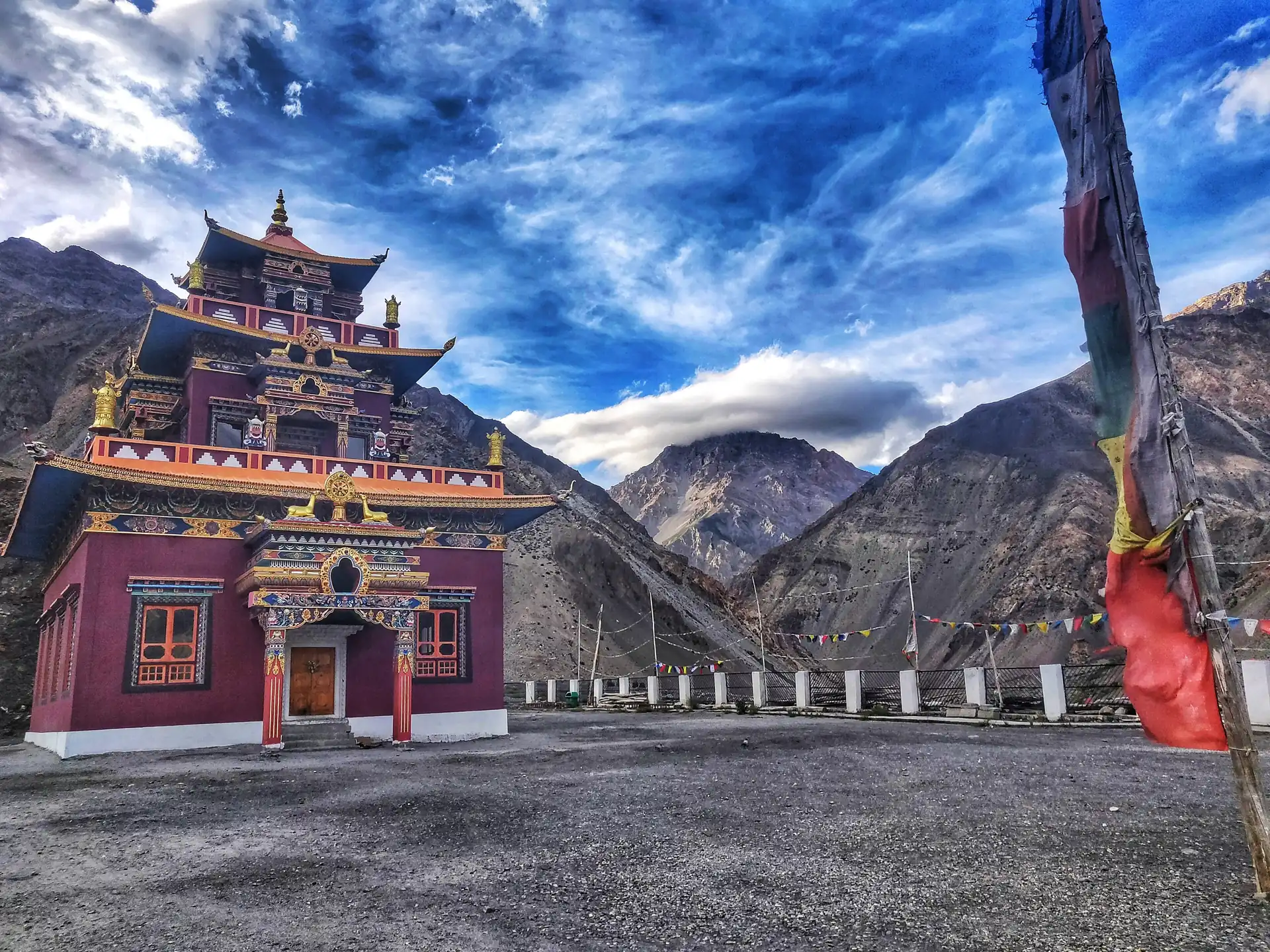 A red and gold monastery building at Gue with prayer flags and a bare mountain behind