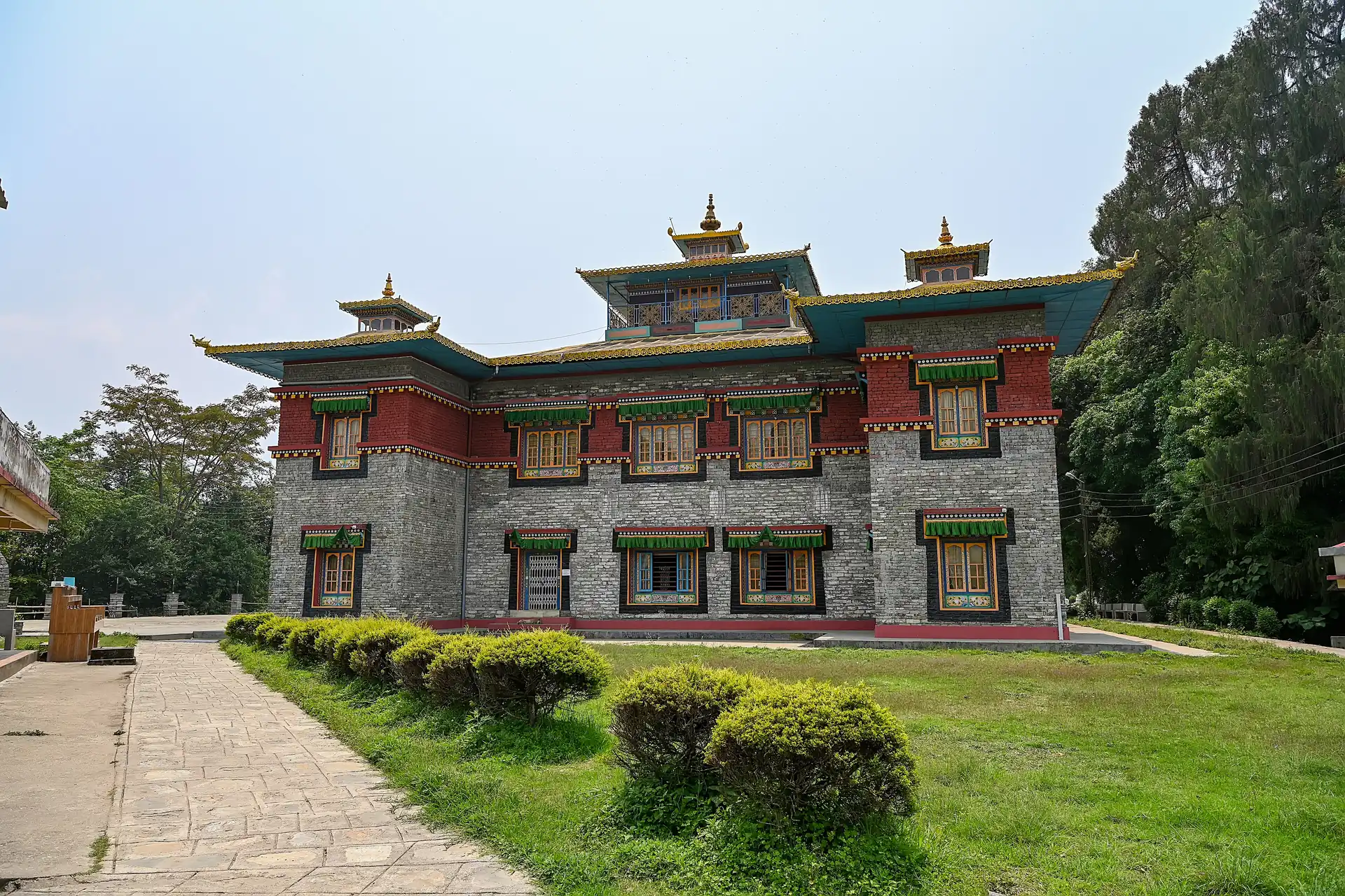 A stone and red monastery building with a green-trimmed blue roof and gilded finials seen across a lawn with clipped bushes