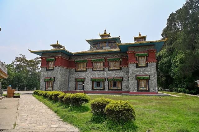 A stone and red monastery building with a green-trimmed blue roof and gilded finials seen across a lawn with clipped bushes