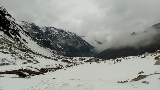 A snow-covered valley below dark mountains under low grey cloud at Sela Pass