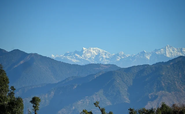 Snow peaks rising above layers of blue forested ridges, seen from Dhanaulti