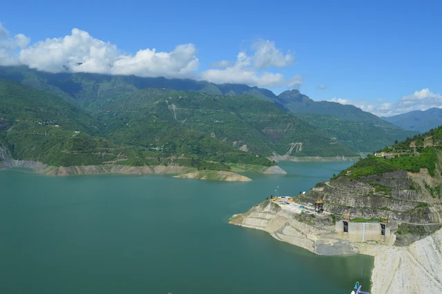 The green waters of the Tehri reservoir winding between forested hills, with the dam's grey wall on the right