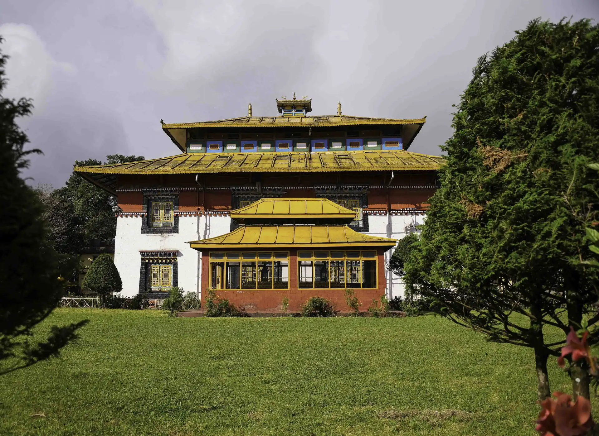 The Tsuklakhang royal chapel with its layered golden roofs and white walls seen across a green lawn and a clipped tree