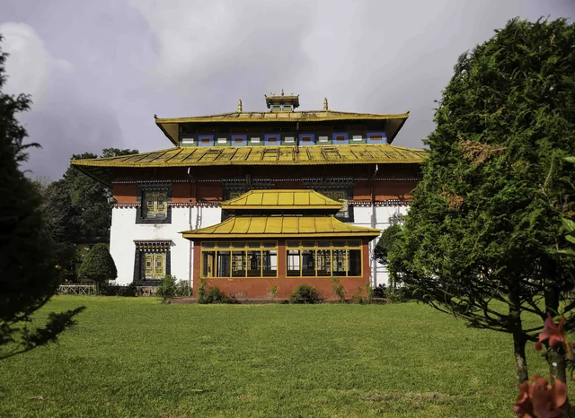 The Tsuklakhang royal chapel with its layered golden roofs and white walls seen across a green lawn and a clipped tree