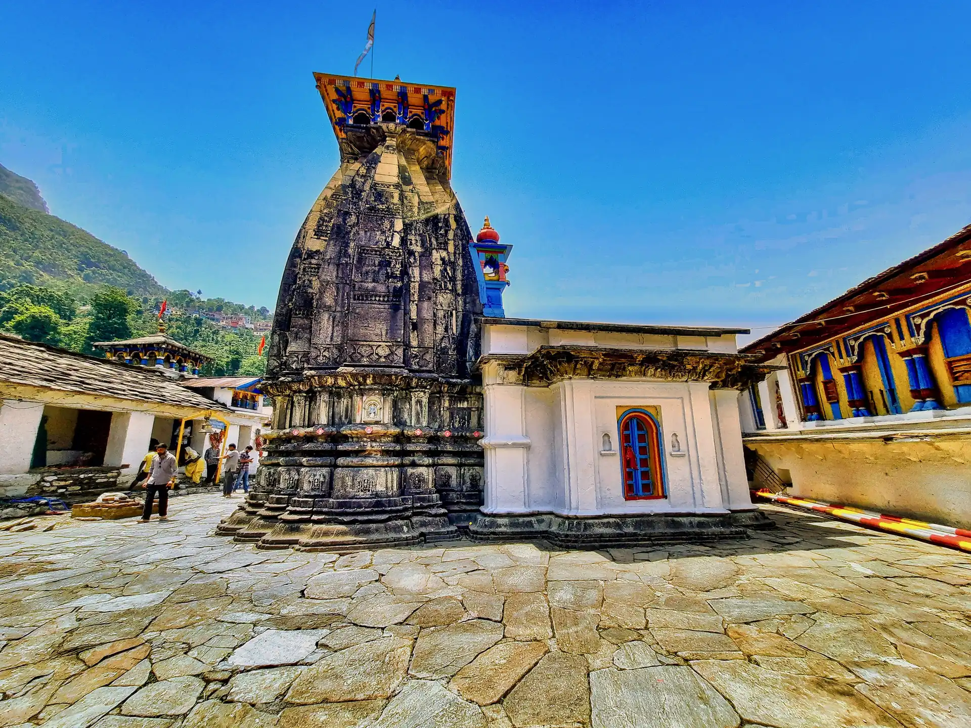 The grey stone shikhara of the Omkareshwar Temple beside a blue-walled shrine in a flagged courtyard under a deep blue sky