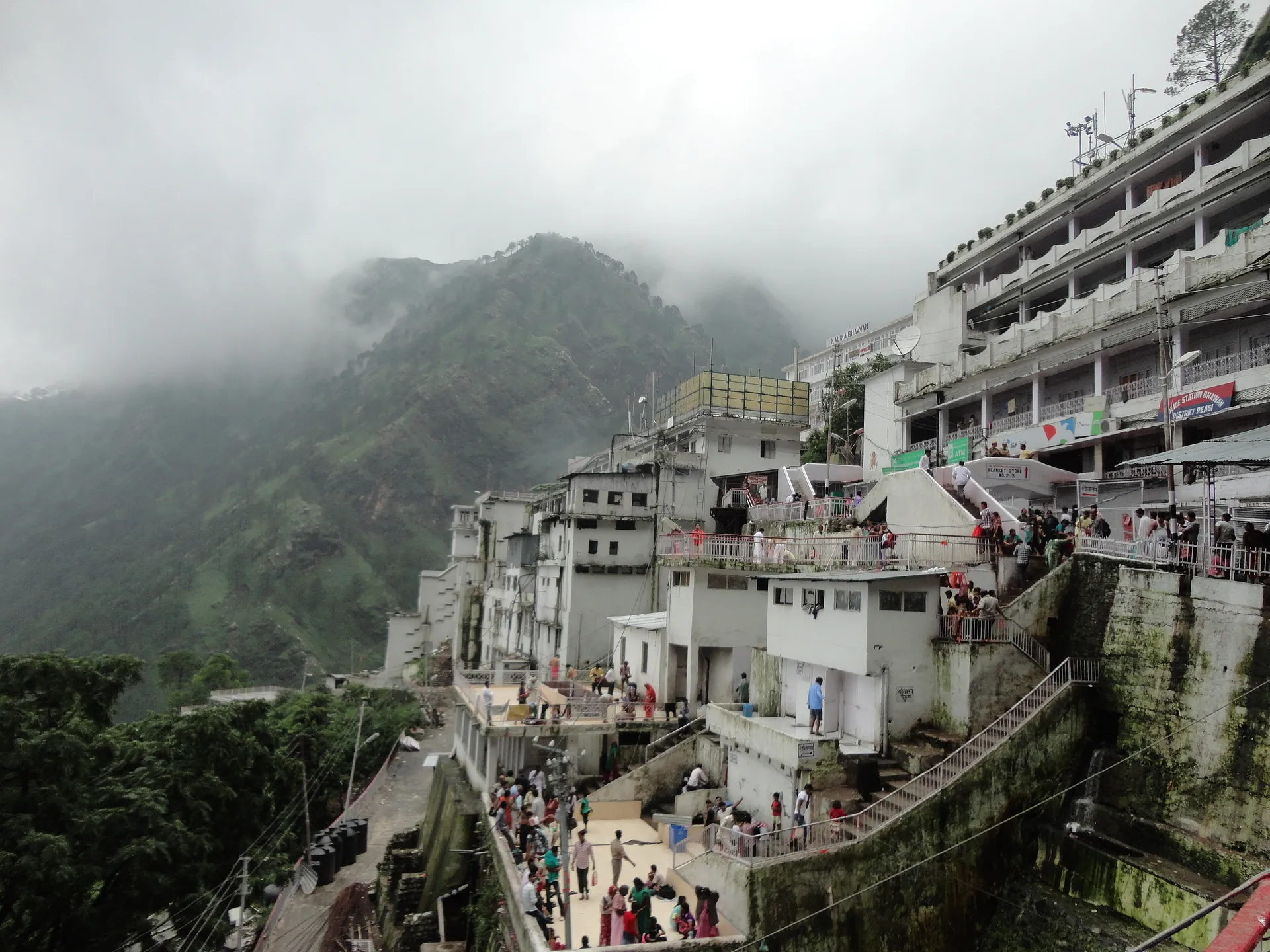 The tall white Bhawan buildings and the stepped path beside them, with mist on the forested hills