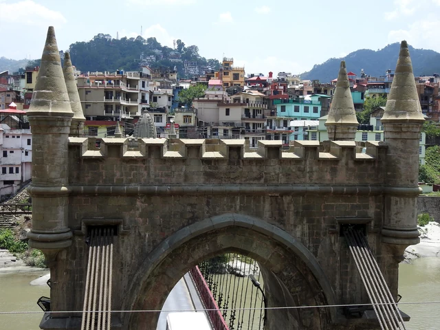 The castle-like stone tower of Victoria Bridge at Mandi, with turrets, an arched gateway and the town's houses behind