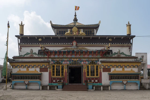 The painted, multi-tiered front of Yiga Choeling Monastery with gilded finials, red windows and a flag above the entrance