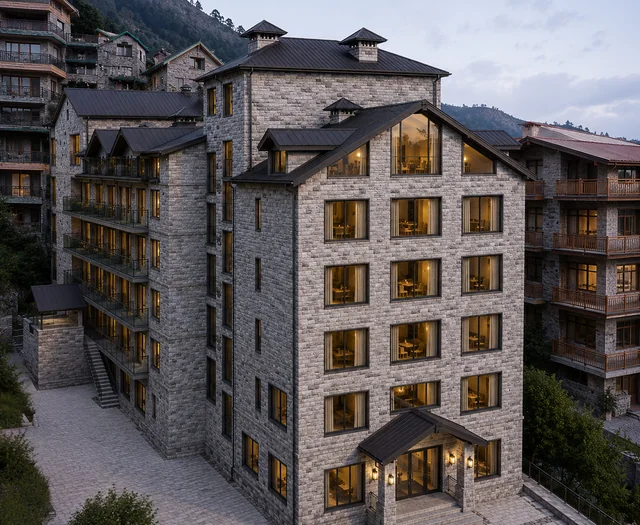 A six-storey stone hotel with dark metal roofs, lit at dusk
