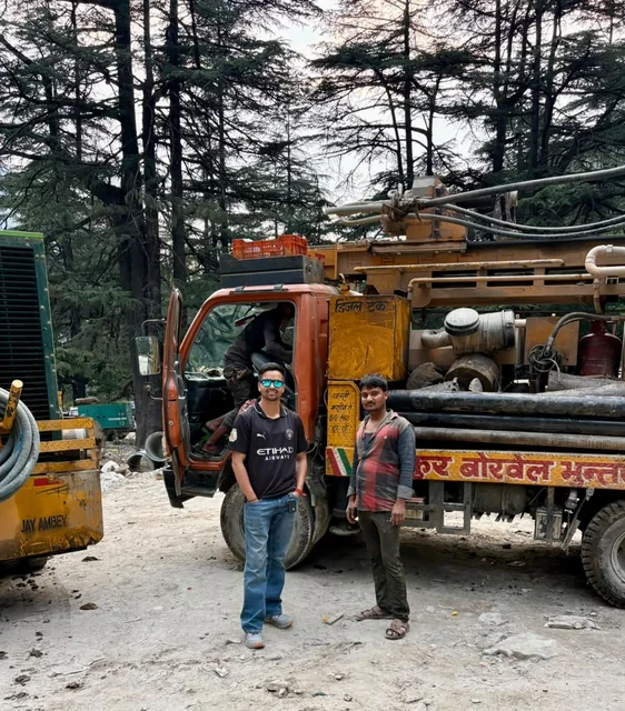 The rig and two of the crew standing in front of it under the deodars