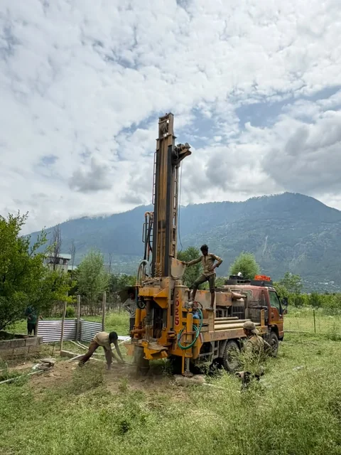 The rig drilling in open ground below the ridges, a man standing on its deck