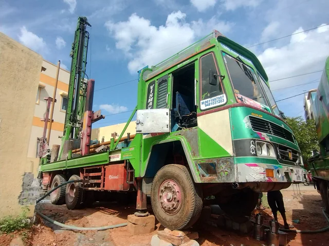 A truck-mounted borewell rig in Bengaluru up on its levelling jacks, wheels off the ground, its mast raised at the tail