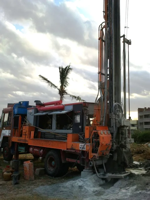 A truck-mounted rig drilling a borewell in India, water and mud running from the hole